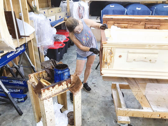 <p>Shane Vickery applies wood stain to a casket in the Finishing Shop. Later, she will install locally made fabric in the casket’s interior.</p>