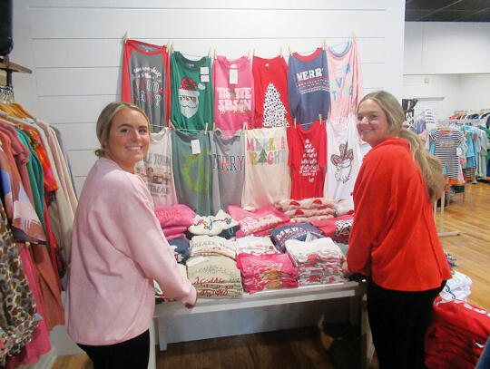 <p>Alex Farmer (left) and Bailey Farmer stock Christmas apparel at the 84 West store on Central Ave.</p>